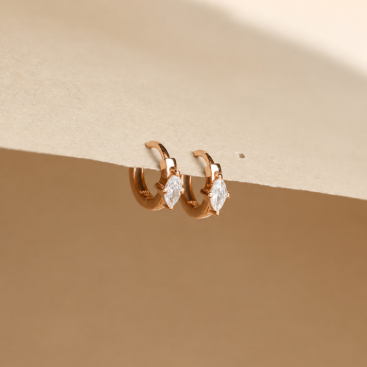 Rose gold hoop earrings with marquise-shaped gemstones on a beige background